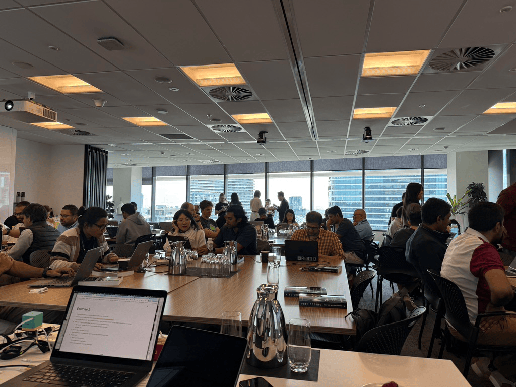 Engineers working at long tables in a glass-walled corporate room during a Vibe Coding workshop